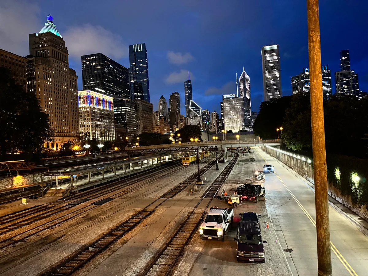 Nighttime panoramic view of Chicago, Illinois skyline with illuminated skyscrapers seen from above train tracks