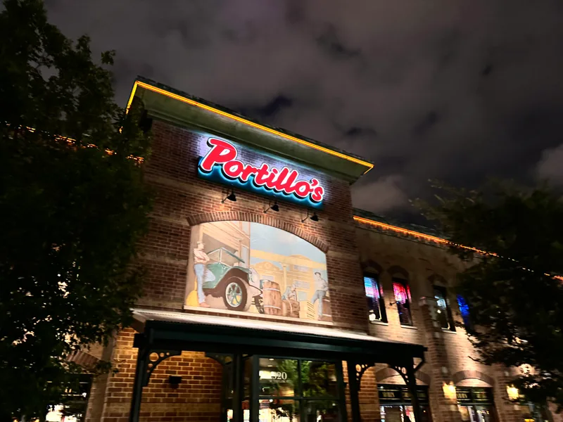 Nighttime exterior of Portillo's restaurant in Chicago, Illinois, with vintage neon sign and car mural