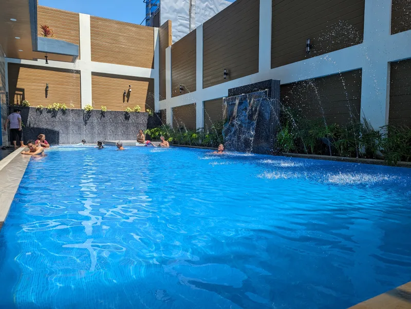 People swimming and playing in the Avery Ridge Resort pool in Pansol, Laguna with an active waterfall on a sunny day.