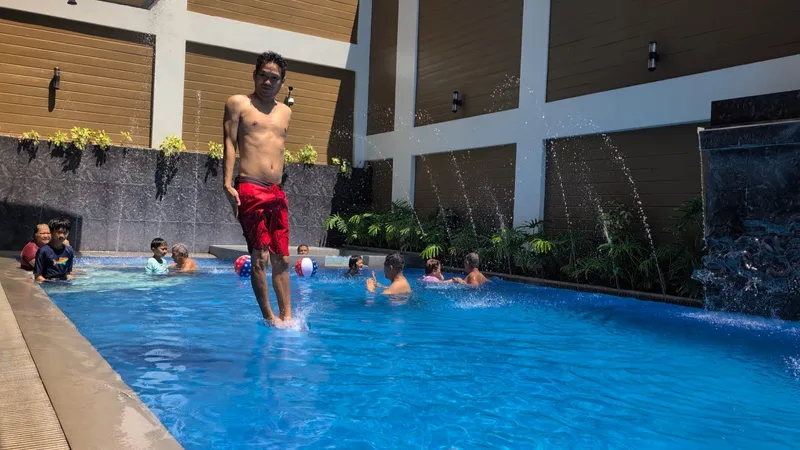 Man in red shorts mid-air jumping into a bright blue swimming pool at Avery Ridge Resort in Pansol, Laguna, with splashing water.