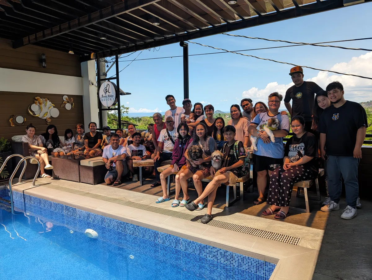 Large family group posing by the swimming pool at Avery Ridge Resort in Pansol, Calamba, Laguna with panoramic green hills in the background.